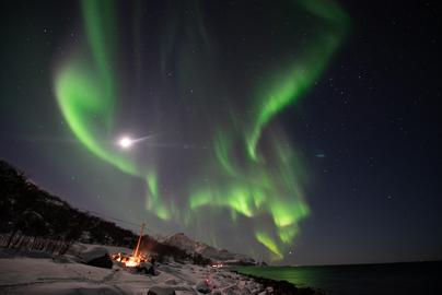 Northern lights and the moon over the campfire by the fjord
