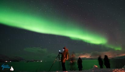 Aurora photographers under the sky of the Northern Lights, by the fjord