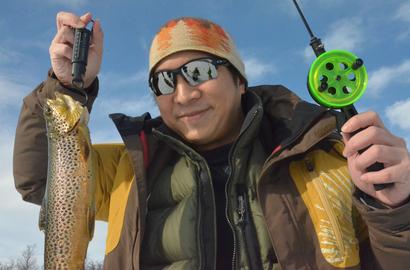 A man with a trout and ice fishing gear.